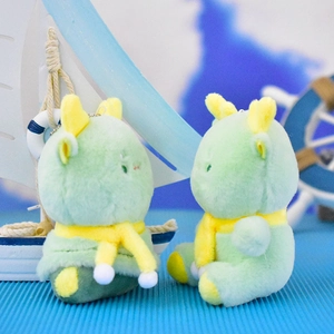 Close-up detail of two cute green dragon plush toy keychains with yellow scarves