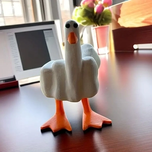 Funny white resin duck giving the middle finger on a wooden desk with a home office background