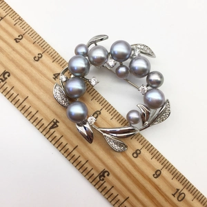 Macro shot of a silver floral brooch with grey pearls and zircons on a wooden ruler