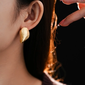 Close-up of a gold shell-shaped textured earring worn by a model in a warm side light