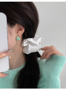 Close-up of a model wearing mint green C-shaped resin earrings and a white satin scrunchie