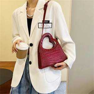Detailed view of red heart-shaped shoulder bag with crocodile texture on white suit