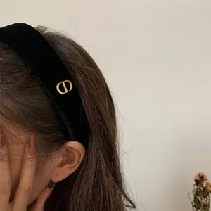Detail of a black velvet headband featuring a gold metal letter logo on the side profile