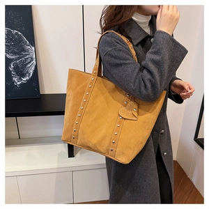 Detail of tan suede tote bag featuring silver rivets and a matching heart-shaped charm