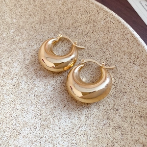 Close-up of polished gold C-shape hoop earrings on a textured ceramic plate