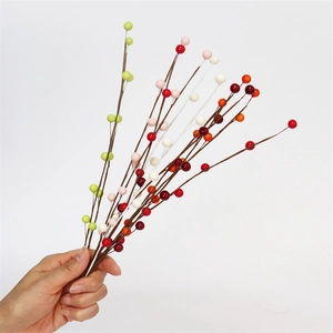 Close-up of hand holding colorful artificial berry branches for festive DIY home decor