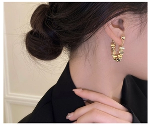 Macro view of gold U-shaped chain earrings with geometric beads on a female model