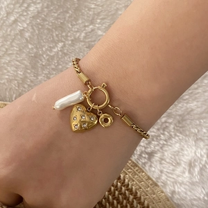 Dettaglio di un ciondolo a cuore dorato e perla barocca su bracciale in metallo