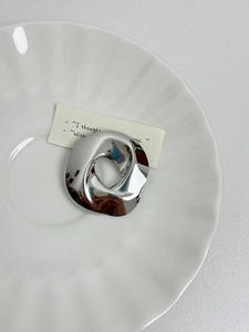 Detail of irregular silver circular brooch on a white textured ceramic dish
