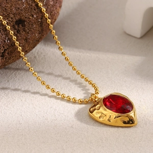 Close-up of 18K gold beaded chain with a red heart-shaped gemstone pendant detail