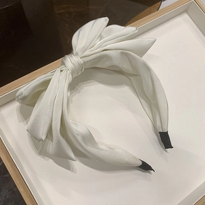 Detail of a white silk triple-layered bow headband on a tray with smooth satin texture