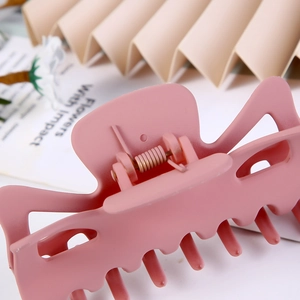 Close-up of a matte pink large hair claw clip with a visible metal spring and geometric design