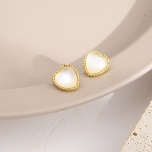 Macro view of heart-shaped pearl stud earrings with beaded golden metal edges