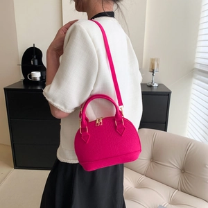 Magenta embossed leather shell bag worn by model in a modern interior setting