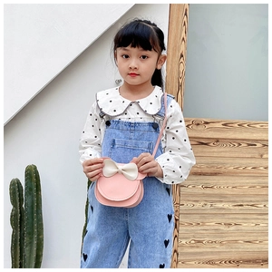 Detail shot of a pink mini crossbody bag with a cream bow on a girl's denim jumpsuit