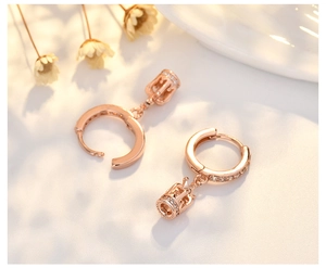 Macro shot of rose gold crown earrings with sparkling crystals on a cream background