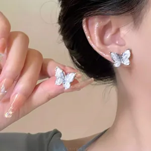 Detail of silver butterfly stud earring with shimmering white wings on model's ear