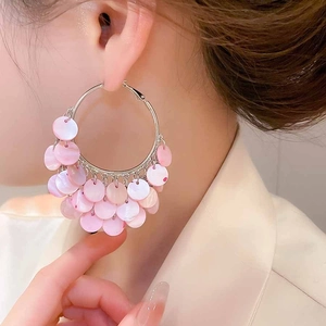 Close-up of silver geometric hoop earrings with shimmering pink shell sequin tassels