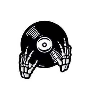 Detail view of enamel pin with black vinyl record held by white skeleton hand bones