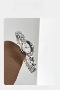 Detail of silver floral bracelet watch with oval dial on brown textured fabric