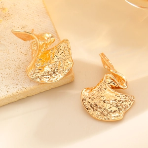 Gros plan de boucles d'oreilles éventail dorées avec texture martelée sur pierre