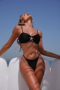 Detail of black bikini top featuring a golden starfish accent against an ocean backdrop