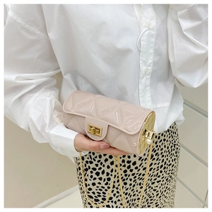Detail of beige quilted cylindrical bag with gold chain, square lock, and side pearls