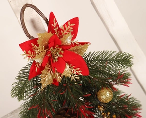Close-up of red silk poinsettia with golden glitter leaves and ornaments on wood