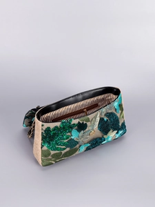 Macro view of floral embroidery and green beadwork on a beige woven shoulder bag