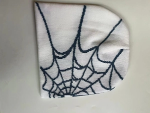 Close-up detail of white knitted beanie featuring black spider web jacquard pattern