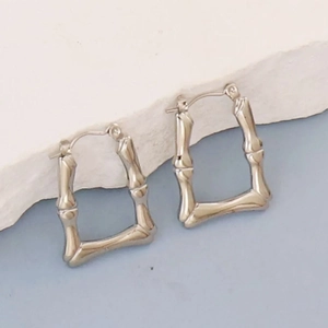Detail of silver bamboo textured geometric earrings on white stone display base