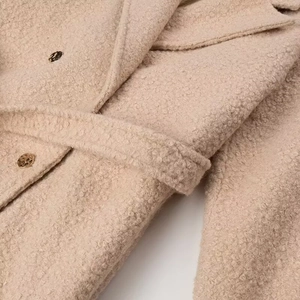 Detail of beige sherpa wool coat showing textured fabric with metallic button and belted waist
