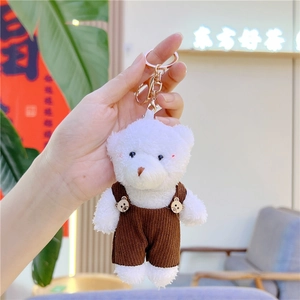 Detalle de llavero de oso de peluche blanco con peto de pana marrón y cierre de mosquetón dorado