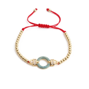 Macro detail of red string bracelet with gold beads and turquoise zircon pendant