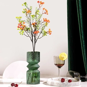 Artificial red berry stems in a green embossed glass vase on a marble tray decor