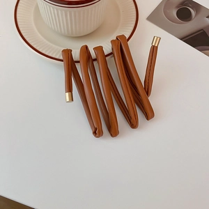 Brown faux leather hair tie with gold metal tips shown in a warm lifestyle setting
