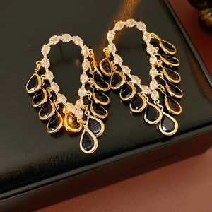 Close-up of golden chandelier earrings with sparkling crystals and black teardrop gems