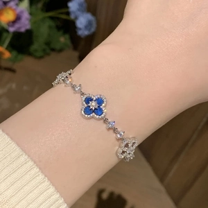 Macro detail of silver four-leaf clover bracelet with blue inlay and crystals on wrist