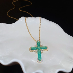 Vue macro du pendentif croix en or avec pierre verte sur un plateau coquillage blanc
