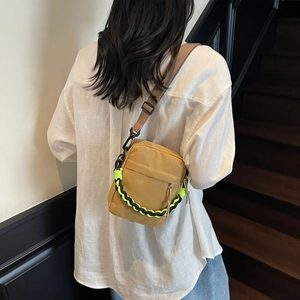 Male model wearing khaki canvas crossbody bag with fluorescent green chain detail on stairs