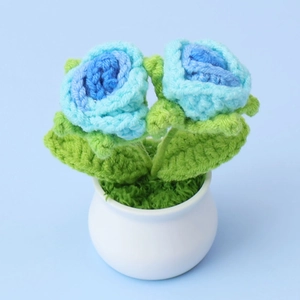 Top view of handmade crochet blue roses in a white ceramic pot with green leaves