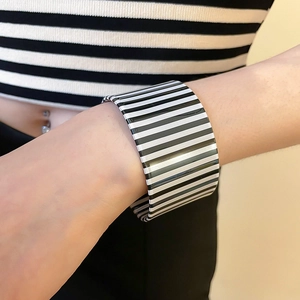 Close-up of wide acrylic bangle with black and white stripes on model wrist