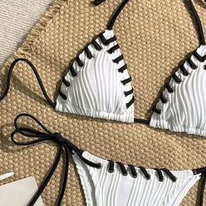Detail of white ribbed bikini featuring black lace-up ties and metallic grommet accents