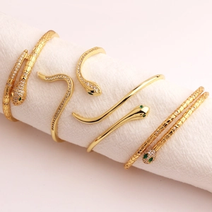 Macro shot of gold snake bracelets with white zircon and green crystal eyes details