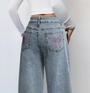 Detail van roze strikborduursel op de achterzak van een lichtblauwe wijde jeans