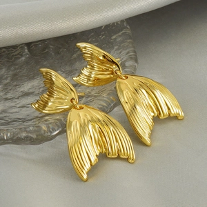 Golden fish tail dangle earrings with textured stripes on silk and glass background