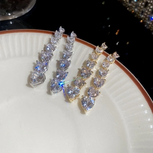 Macro detail of 18K gold and silver plated long heart drop earrings with zircon in a tray
