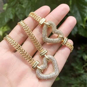 Chunky gold chain necklace with a heart pendant in a crystal setting shown on a palm