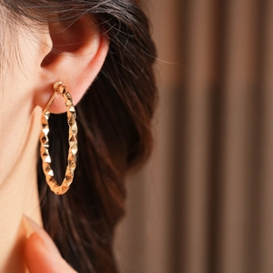 Detailed view of large gold geometric C-shaped hoop earrings on model featuring diamond-cut texture