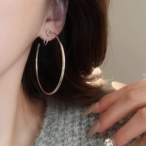 Close-up of a silver-toned large circular hoop earring worn on an ear with a polished finish